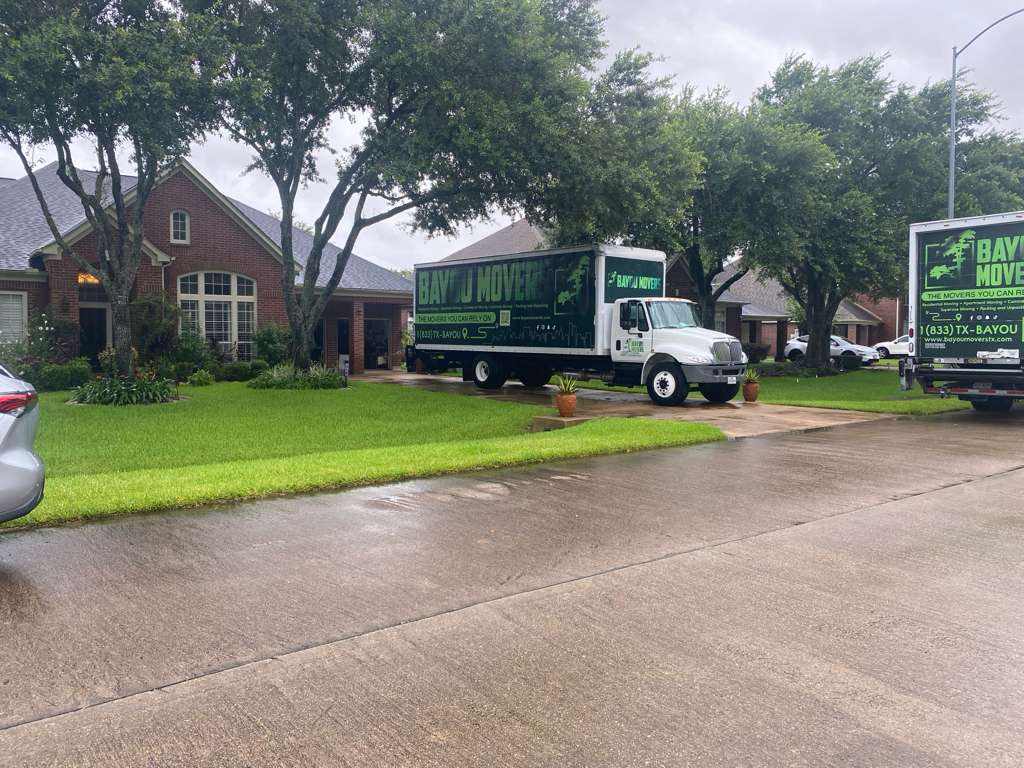 Two Bayou Movers trucks outside a brick home